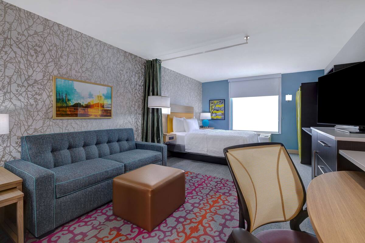 A hotel room with a sofa, a bed, a desk, a TV, and a patterned rug.