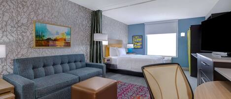 A hotel room with a sofa, a bed, a desk, a TV, and a patterned rug.