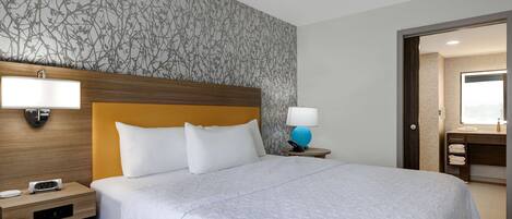 A hotel room with a large bed, a wooden headboard, a nightstand with a lamp, and a wall with a floral pattern.