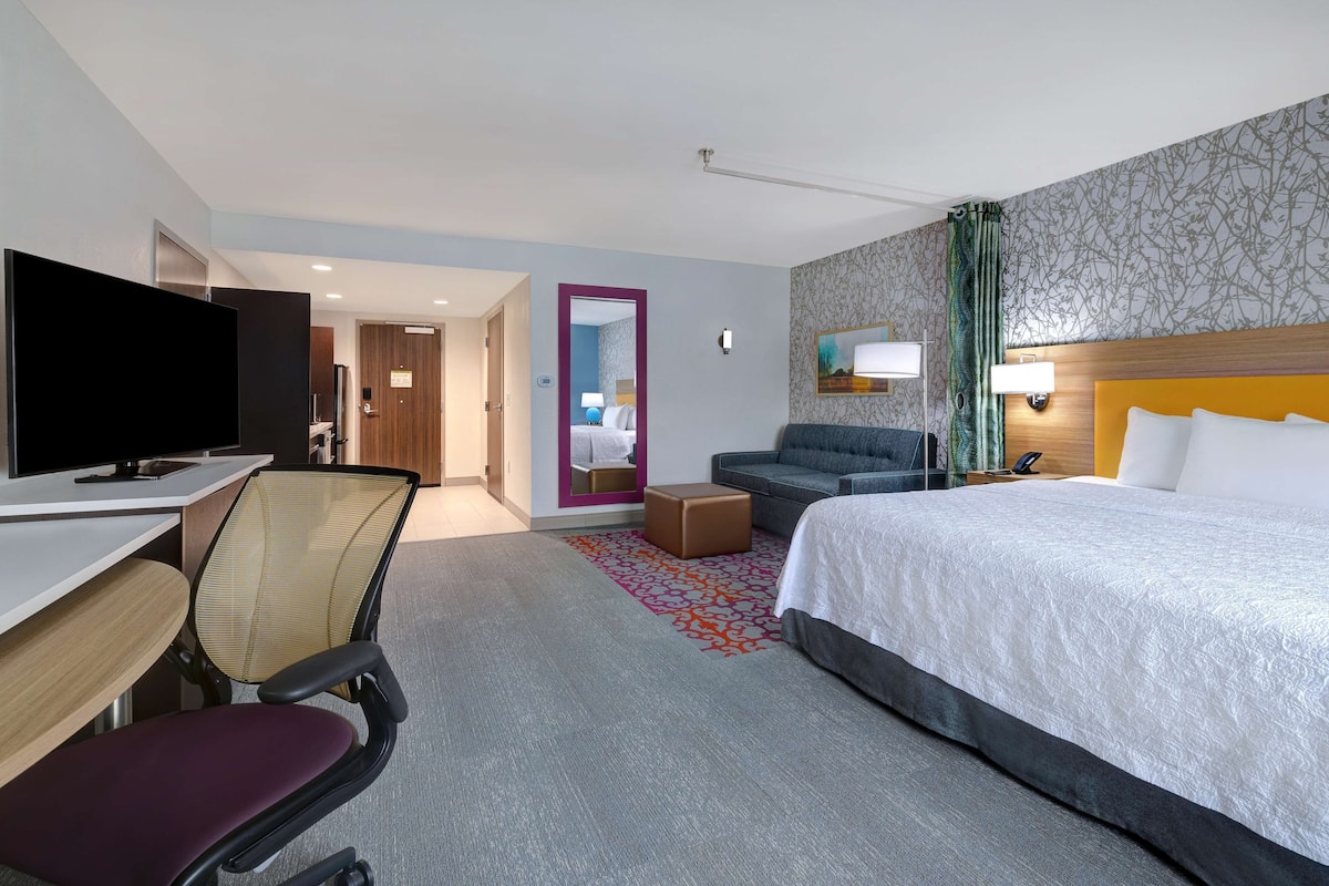 A hotel room with a bed, a desk with a computer, a chair, a sofa, and a television.