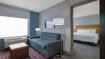 A hotel room with a sofa, a bedside table, a lamp, a patterned rug, and a bed with a headboard.