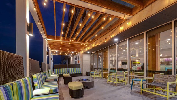 An outdoor seating area with striped sofas, round tables, and yellow chairs. - Home2 Suites by Hilton Wilkes-Barre (Wilkes-Barre)