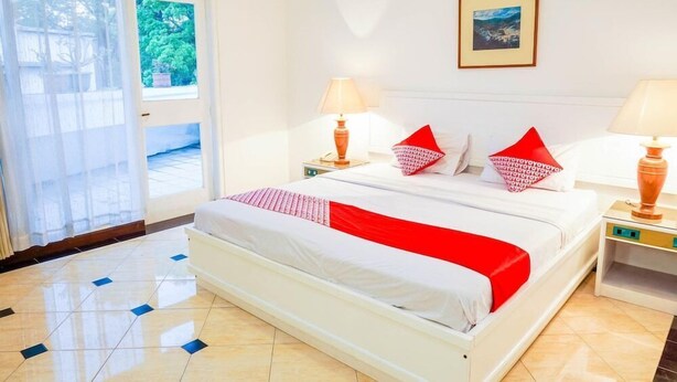 A hotel room with a bed, two bedside lamps, a picture on the wall, and a view through the window. - Hotel Utari Dago (Bandung)