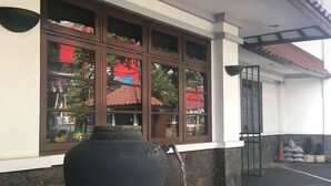 A large black pot on a pedestal, a window with reflections, and a stone wall. - Hotel Utari Dago (Bandung)