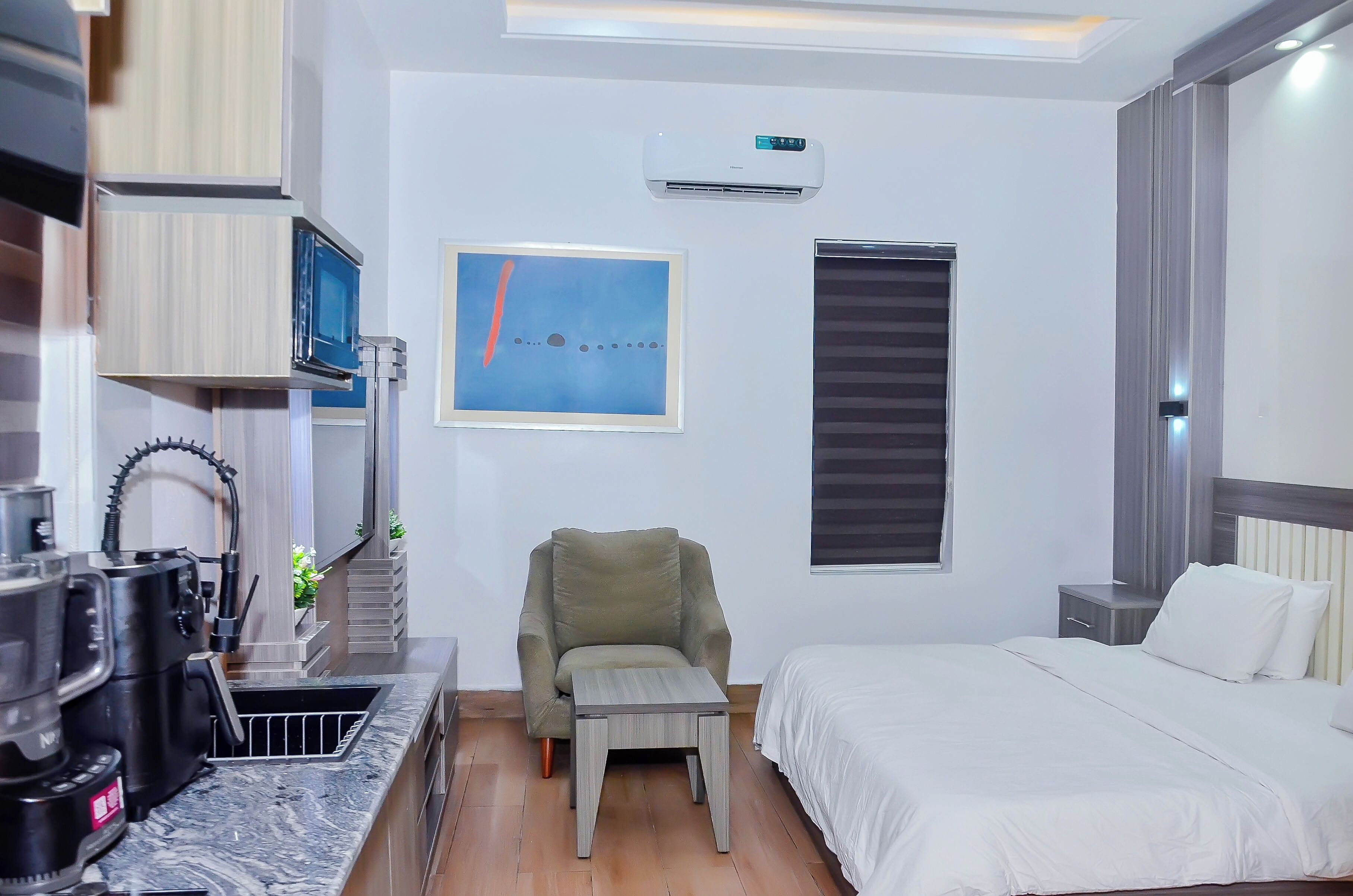 Una habitación de hotel moderna con cama, sillón, mesita, microondas y aire acondicionado.