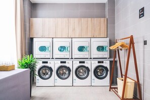 A laundry room with six washing machines and a wooden cabinet above them.