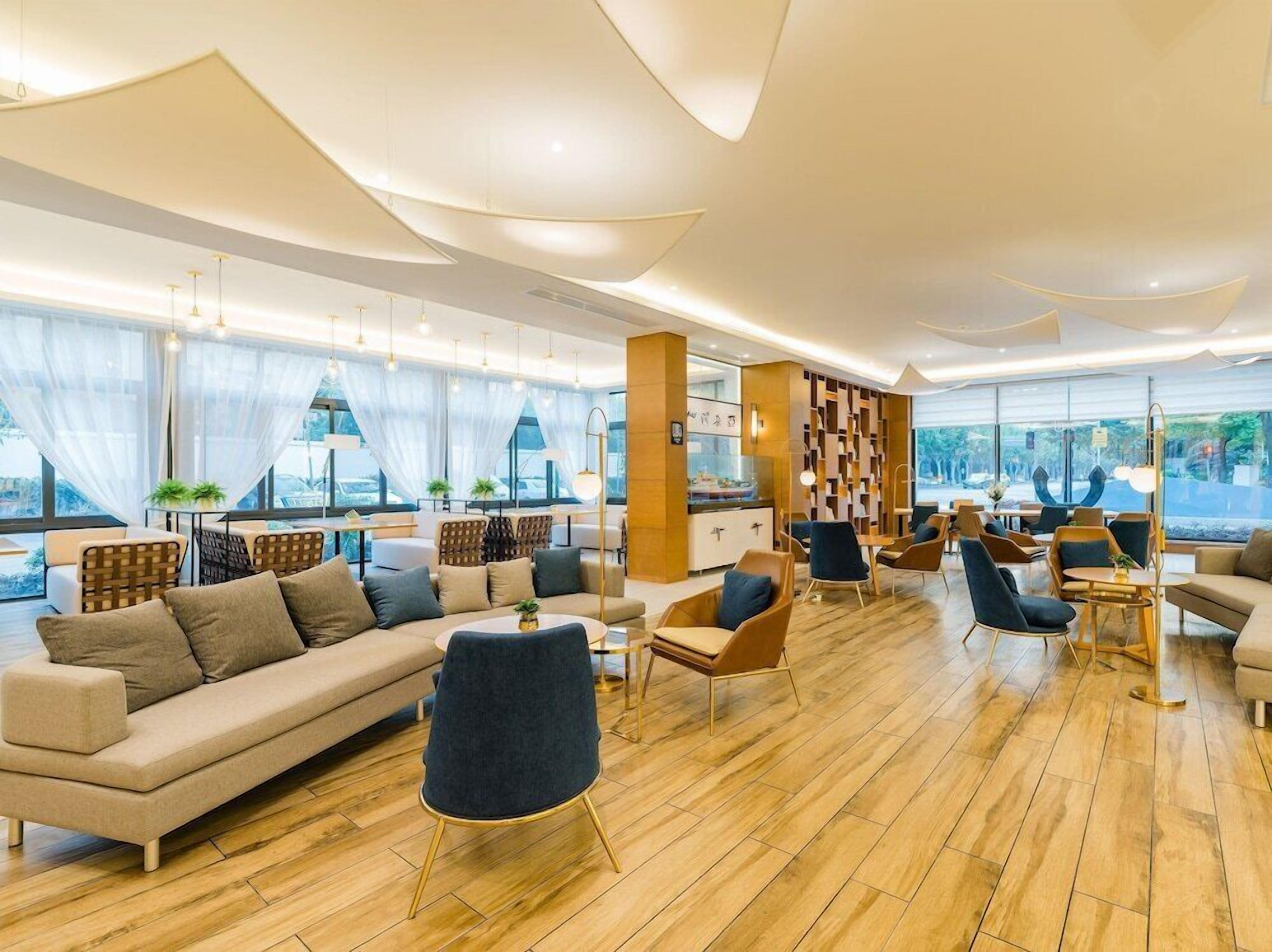 Un hall d’hôtel moderne doté d’un grand espace salon, d’un comptoir d’accueil et offrant une vue sur l’extérieur.