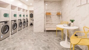 A laundry room with multiple washing machines, a drying rack, and a small table with chairs. - Atour Hotel (Jiaxing)