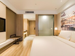 A modern hotel room with a large bed, a desk, a chair, a TV, and a painting of a bridge.