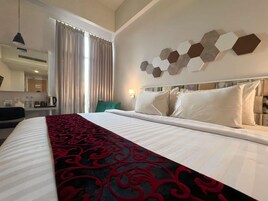 Quarto de hotel com uma cama grande, uma escrivaninha com cadeira, um espelho e uma janela com cortinas.