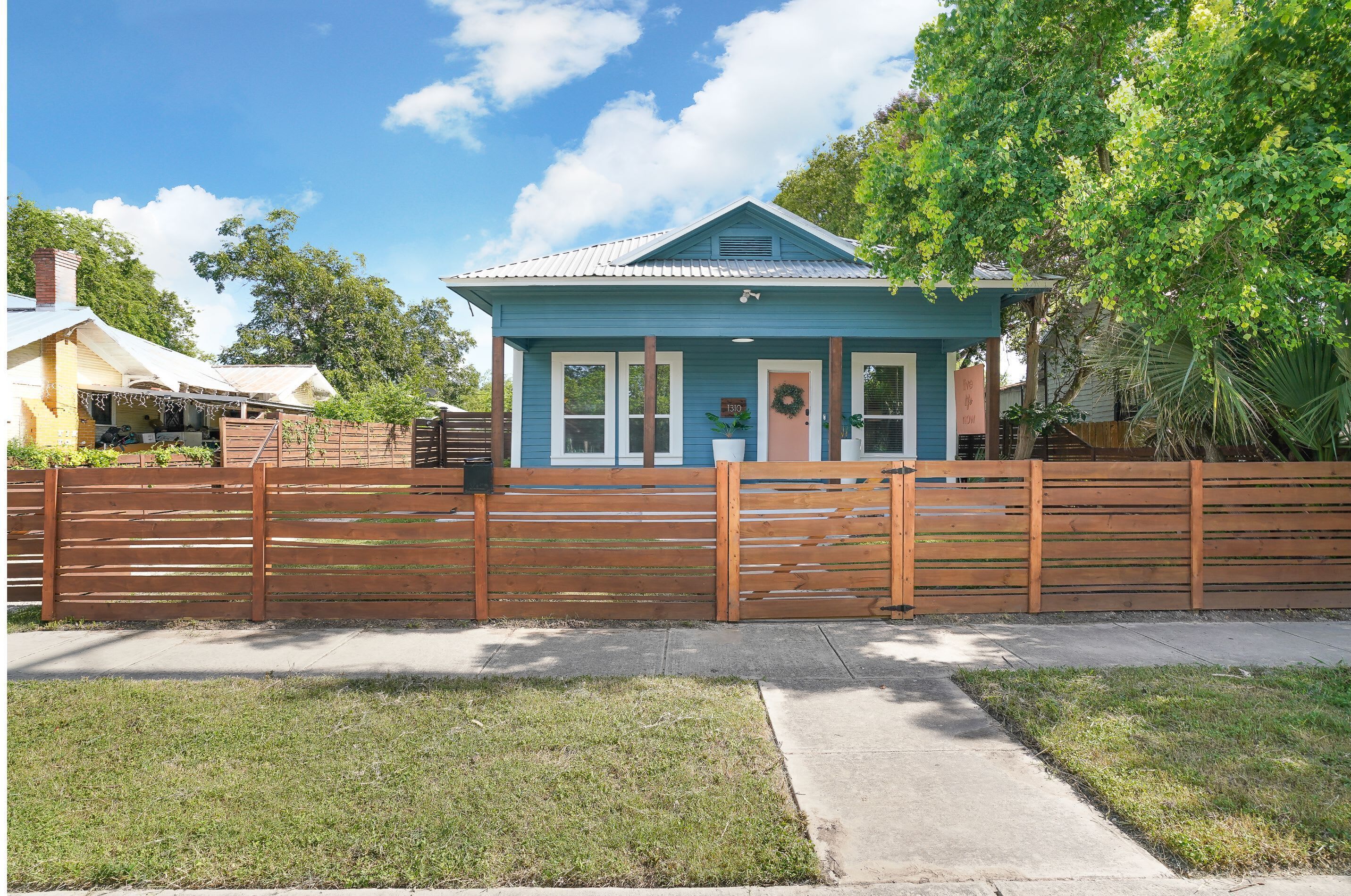 Une maison de plain-pied à l’extérieur bleu, avec une clôture en bois devant.
