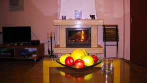 Una sala de estar con chimenea, televisor y frutero sobre la mesa.