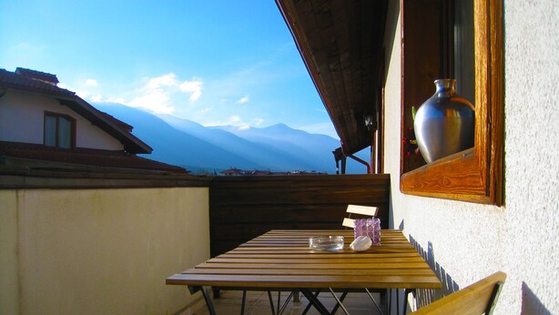 Una mesa de madera con un jarrón y una vela en un balcón con vistas a montañas.