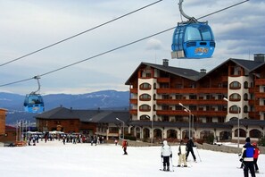 Ein Skigebiet mit einer Seilbahn, einer großen Lodge mit mehreren Balkonen und verschneiter Landschaft.