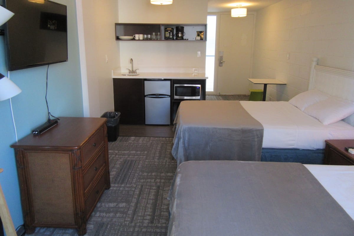 Una habitación de hotel con dos camas, un kitchenette pequeño, un televisor y un escritorio.