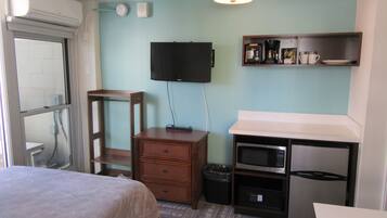 A compact hotel room with a bed, a desk with a microwave, a television, and a small kitchenette.