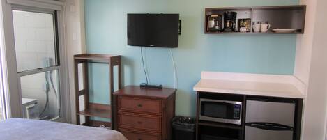 Habitación de hotel compacta con cama, escritorio con microondas, televisión y una pequeña kitchenette.