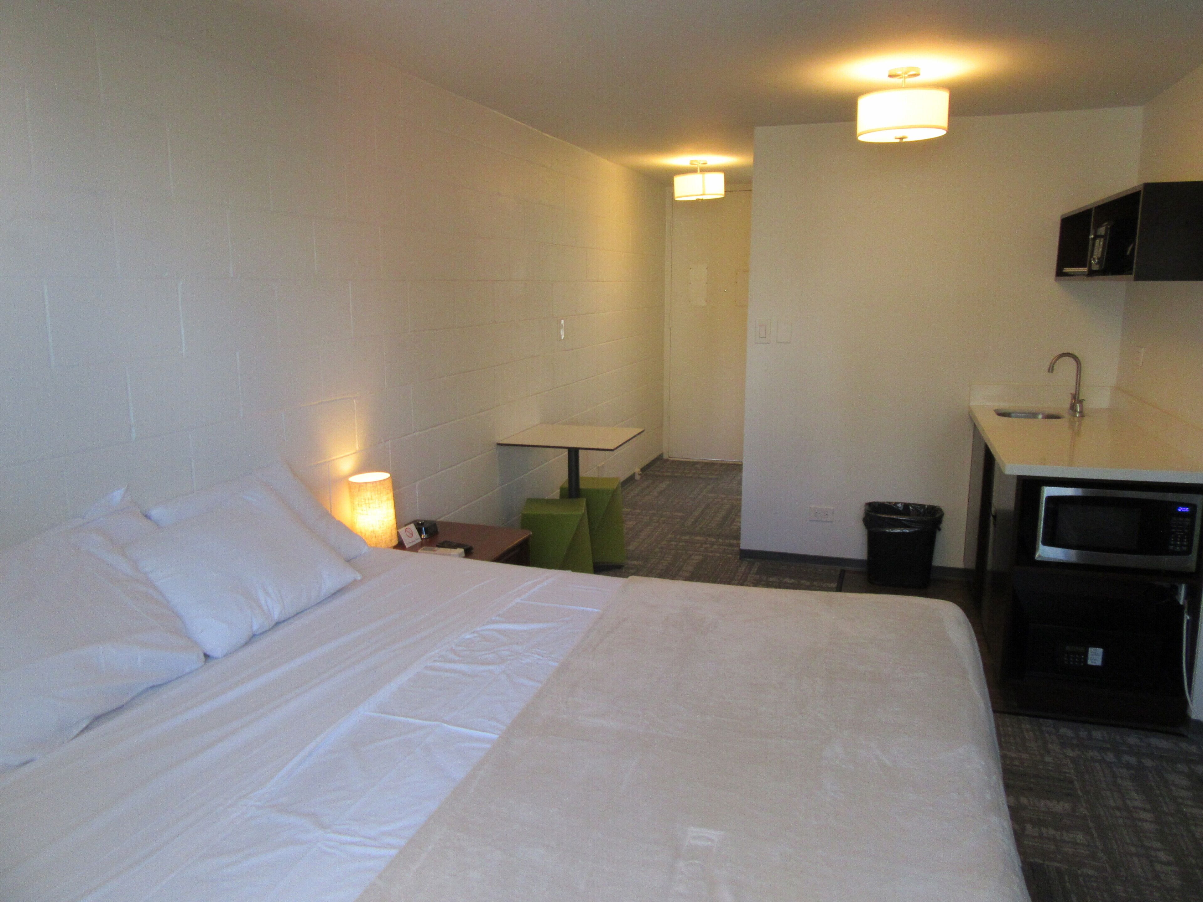 A hotel room with a bed, a desk, a microwave, and a small sink.