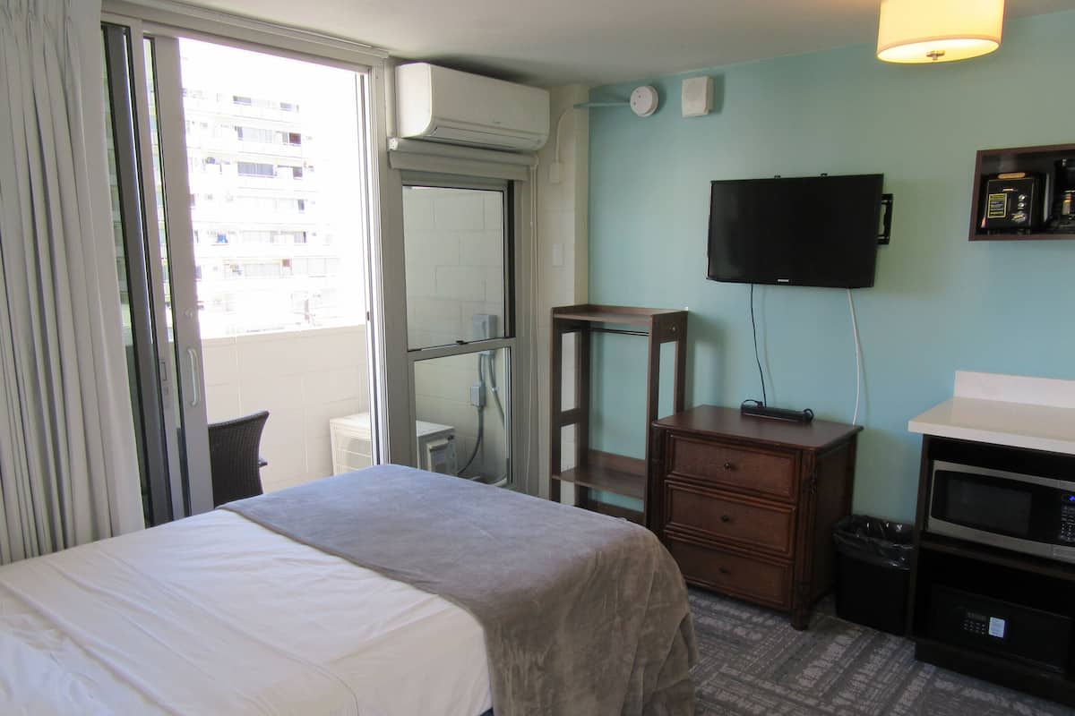 Una habitación de hotel con una cama, un escritorio, un televisor y un ventanal con cortinas.