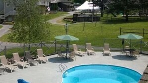 A swimming pool with lounge chairs and umbrellas, surrounded by a grassy area and buildings.