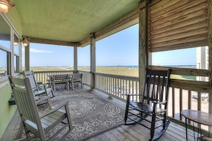 A wooden deck with rocking chairs and a table, overlooking a beach.