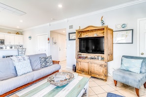 A living room with a sofa, a coffee table, a TV stand, and a dining area with cabinets.