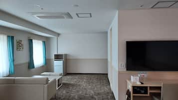 Een hotelkamer met een bank, een televisie, een bureau met een computer en een kleine kitchenette.