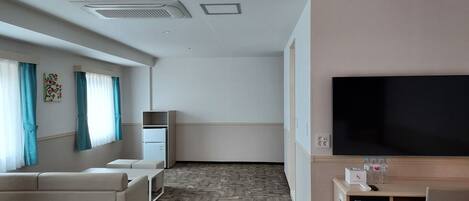Habitación de hotel con sofá, televisión, escritorio con ordenador y una pequeña kitchenette.