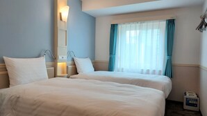 A hotel room with two beds, a window with curtains, a wall-mounted light, and a small table with a bottle. - Toyoko Inn Changwon (Changwon)