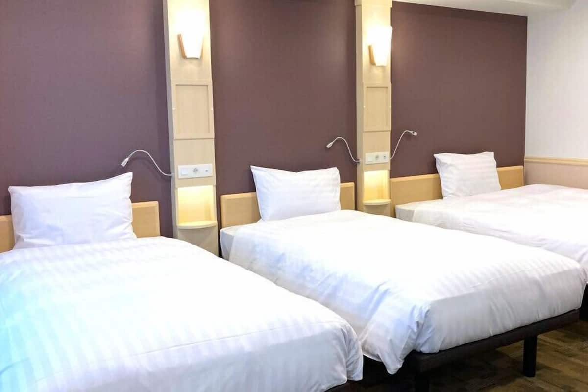 A hotel room with three single beds, each with a headboard and bedside table.
