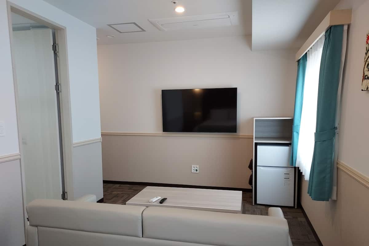 A compact living room with a flat-screen TV mounted on the wall, a small refrigerator, and a sofa.