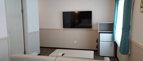 A compact living room with a flat-screen TV mounted on the wall, a small refrigerator, and a sofa.