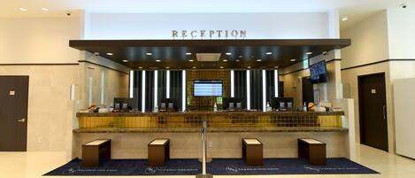 Un área de recepción con un cartel que dice 'RECEPTION', una pantalla digital y un mostrador con una mampara de vidrio.