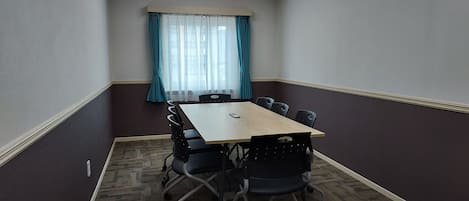 A conference room with a rectangular table, six chairs, a ceiling light, and a window with curtains.