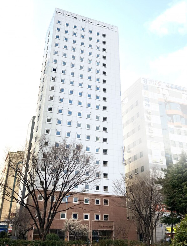 A tall, modern building with a grid of windows, surrounded by trees and other buildings.