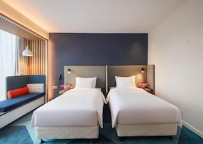 A hotel room with two beds, a seating area with a red cushion, a wall-mounted lamp, and a nightstand with a flower vase. - Holiday Inn Express Shanghai Xuhui Binjiang (Shanghai)