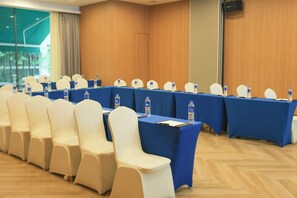 Un salón de conferencias con una larga mesa, sillas blancas y botellas de agua.