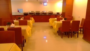 Un restaurante con mesas amarillas y sillas rojas, una cocina al fondo y un suelo limpio y brillante.