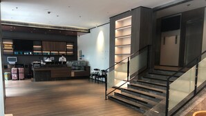 Un moderno vestíbulo de hotel con una recepción, una escalera con barandillas de vidrio y una zona de estar.