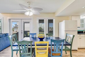 A dining area with a table, chairs, a ceiling fan, and a refrigerator.