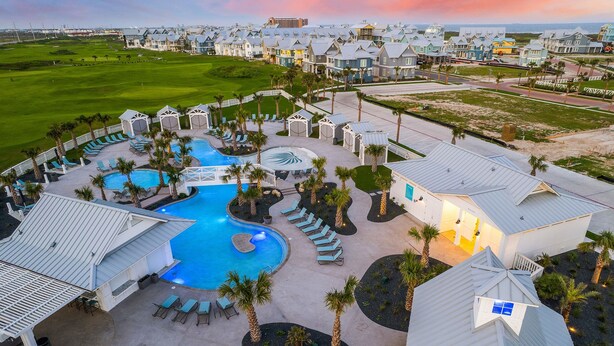 Een resort met een groot zwembad, loungegedeeltes en een golfbaan op de achtergrond.