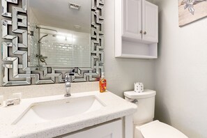 A bathroom with a white sink, a mirror with a geometric frame, a toilet, and a cabinet above the toilet. - Gulf & Gather | 2 Resort-View Balconies | Heated Pools, Tennis, Beach Access (South Padre Island)