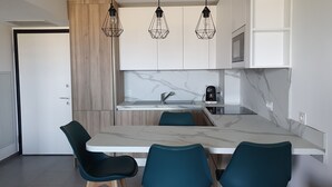 A modern kitchen with a marble countertop, a built-in stove, and a coffee maker. There are three chairs and a wooden cabinet. - Superb T2 apartment with a beautiful view of the sea and the Bloody Islands (Grosseto-Prugna)