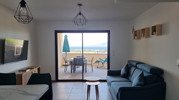 A modern living room with a sofa, a dining table, and chairs. There is a balcony with a view of the sea. - Superb T2 apartment with a beautiful view of the sea and the Bloody Islands (Grosseto-Prugna)