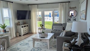 En stue med loftventilator, fjernsyn, sofa, sofabord og udsigt til baghaven.
