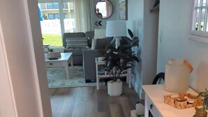 En gang der fører til et opholdsområde med en sofa, et sofabord og en plante. Der er et tæppe på gulvet og et vindue med gardiner.