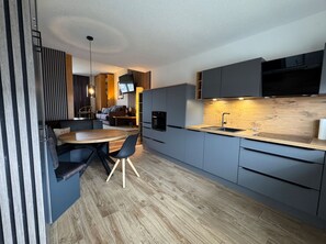 A modern kitchen with grey cabinets, a wooden dining table, and a built-in oven. - Just 100 m from the beach, apartment with a balcony - Apt. Eldena FeWo 15 - Apartments (Middelhagen)