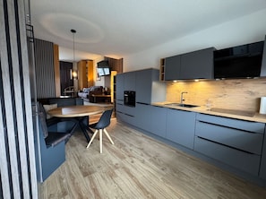 A modern kitchen with grey cabinets, a wooden dining table, and a built-in oven.