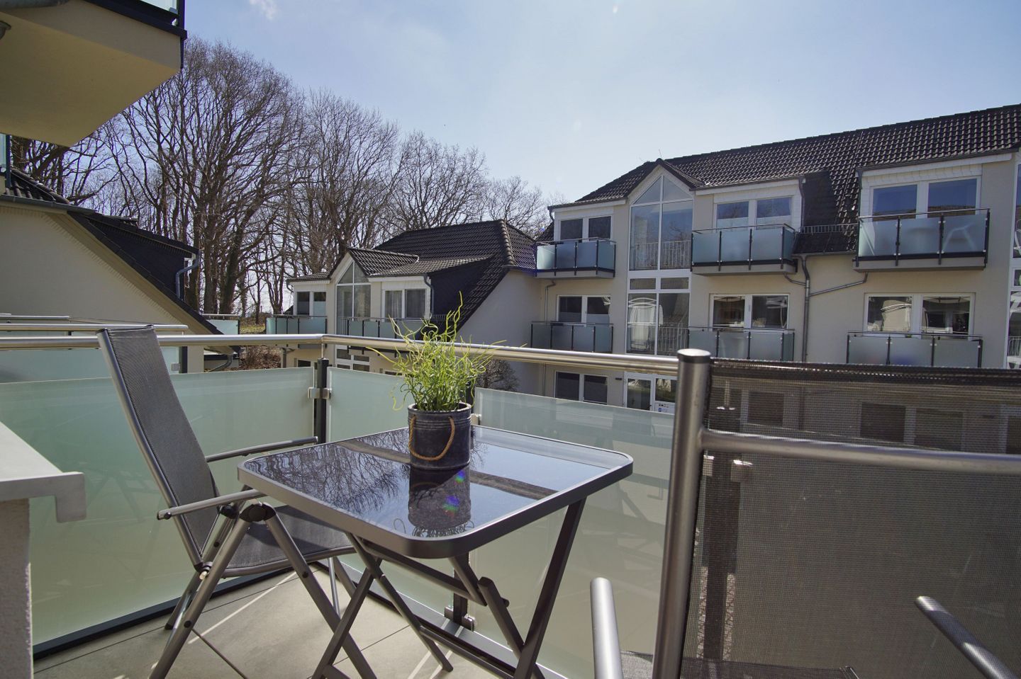 Ein Balkon mit Tisch und Stühlen, einem Blumentopf und Blick auf Wohnhäuser.