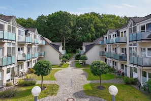 A row of modern apartment buildings with balconies, a central pathway, and well-maintained greenery.